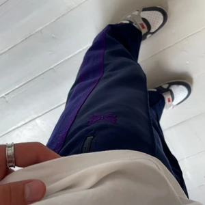 Needles trackpants - Ett par trackpants från Needles japan i blå och lila colorway. Relaxed/baggy fit på benen men bra passform i midjan. Storlek M men passar S på grund av resorband och justerbara snören i midjan. I bra skick, knappt använda dock utan kvitto men lätta att legitchecka.