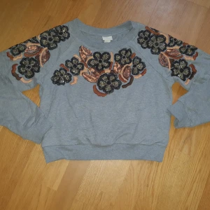 H&M Trend sweatshirt med paljetter - Sweatshirt från H&M Trend med paljetter både fram och bak i storlek 38. Tillverkad av 100% bomull (exklusive paljetter). Handtvätt. Den är något boxig och kortare i livet, hamnar ungefär ovanför höftbenen för mig som är 164 cm lång. Använd ett fåtal ggr, mycket fint skick. Ordinarie pris 499 kr. 