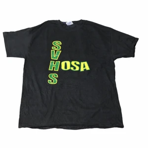 SVHS - Vintage T-shirt - En svart tröja med ett grönt och gult tryck som är från ett college/ en high school i USA. Perfekt för att bland in lite färger i din stil. Köpt på en secondhandbutik i Colorado.