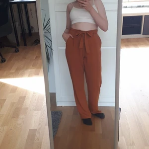 Rostig färgad byxor, storlek 38 - Ett par byxor av polyester. Byxorna har hög midja och raka, vida ben. Nästan oanvända.