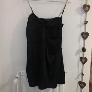Svart miniklänning - Miniklänning från Naanaa (nypris ~400kr) i storlek 42 ( passar 40 också). Säljer för att jag insåg inte att kedjorna va guld och jag har silversmycken :/ använd en gång, väldigt bekväm för att vara en finare klänning. Har korsett detaljer upptill och går till mitt på låren ungefär