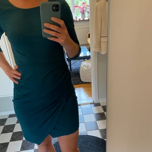 Klänning m rysch. Från Vila strl M.  - Stretchig bomullig klänning med 3/4 ärm med en kjoldel som går lite omlott och är ryschad. Djup u-ringning i ryggen. Från Vila. Strl M. Finns att hämta i Midsommarkransen, Stockholm. 