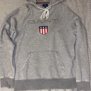 Gant Hoodie - Grå Gant hoodie! Nypris 700kr. Den är använd och har derför några skador (som du ser på bilderna). Den är medium men passar även de som brukar ha small. Så om du är runt 170 så funkar det bra. Men den är för liten för mig som är 184. Plagget är garanterat ditt efter Swish!