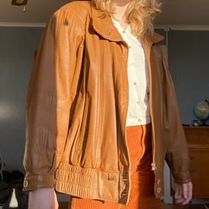 Skinnjacka brun - Äkta läderjacka som i fårskinn. Från 80-talet av märket Saki. Storlek 42. Ljusbrun i färgen. Jag (på bild) är 175 lång och bär vanligen storlek S-M (36-38). Tyget på insidan är ihoplappat på grund av en reva. Skicka ett meddelande för