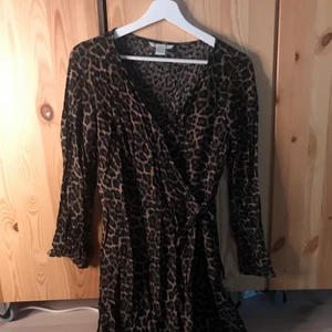 Omlottklänning Leopardmönster - ALDRIG ANVÄND! Omlottklänning från H&M i storlek 36. Leopardmönster och knyte. Långa ärmar och själva klänningen går över knäna. En midiklänninh. Lågt pris pga möts ej upp utan skickar på post och köpare står för frakt! :)