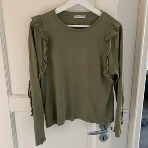 Grön topp med volang  - Tröja med volang. Har en fläck som en får bort. Köpare står för eventuell frakt 