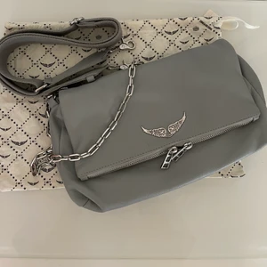 Zadig & Voltaire Väska - Zadig väska i en grå/blå färg i den större modellen.       Använd fåtal gånger men köpt för 2 år sedan.        Original pris: ca 4000 kr. Både band och kedjan ingår. Budgivningen börjar på 1200kr!