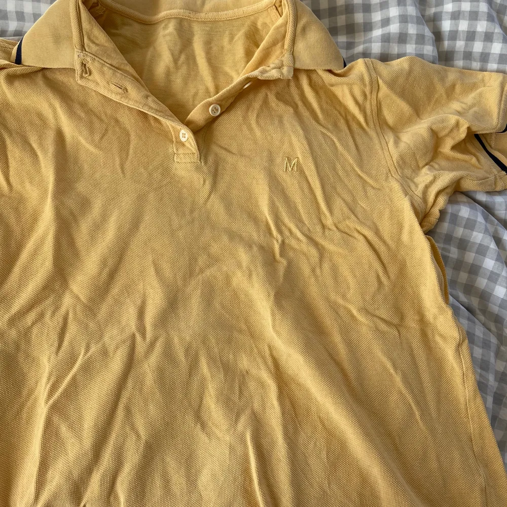 Gul polo T-shirt med två svarta ränder på ärmarna och markerade sömmar, ett broderat M på bröstet. 20kr+frakt. T-shirts.