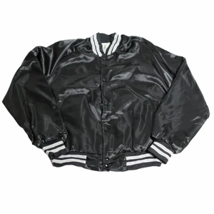 Svart Varsity Jacka - En riktigt fet jacka som är gjort av svart material som är nylon och skyddar därför väldigt bra mot vind och även mot regn. Perfekt för en 90s aesthetic till hösten som är så svår att få tag på. Men med denna jackan för du det!