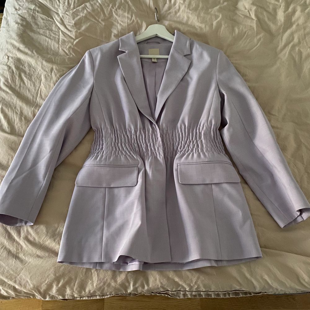 Jättefin ljuslila kavaj från H&M, passar perfekt för en fin sommarkväll. Den är aldrig använd och på mitten av kavajen finns det en smock kant som ger kavajen mer figur! . Kostymer.
