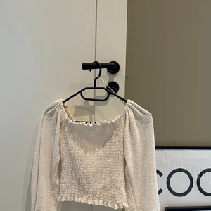 En vit croppad smocktröja i vitt Strl S - Tröjan jag säljer är en vit smocktröja/blus ifrån Bikbok, i amrarna är den pösig med lite kortare ärm och i midjan sitter den tajt så den framhäver ganska mycket midja. Jag har inte havt så mycket användning för den derför säljer jag den. Tröjan är i storlek S men är lite tajt så den kan passa XS också☺️