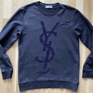 Saint Laurent Sweatshirt  - Mörkblå sweatshirt från YSL med stor logo i flock print. Storlek large men passar även medium. Tröjan är överlag i bra skick men det finns två defekter. Svaga fläckar efter blekning uppe vid kragen (bild 2) och viss slitning längst ner på logon (bild 3). 