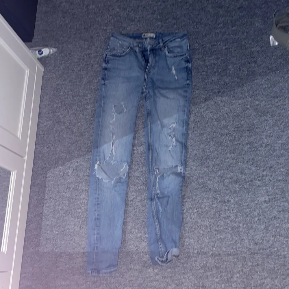Ett par blåa jeans med hål på knäna å även hål i fickorna ibak. Storlek 26. Använda ganska mycket . Jeans & Byxor.