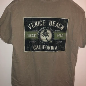Venice Beach T-shirt - Beige/grå T-shirt med Venice Beach tryck. Litet tryck på höger framsida och stort tryck på ryggen. Uppvikta ärmar