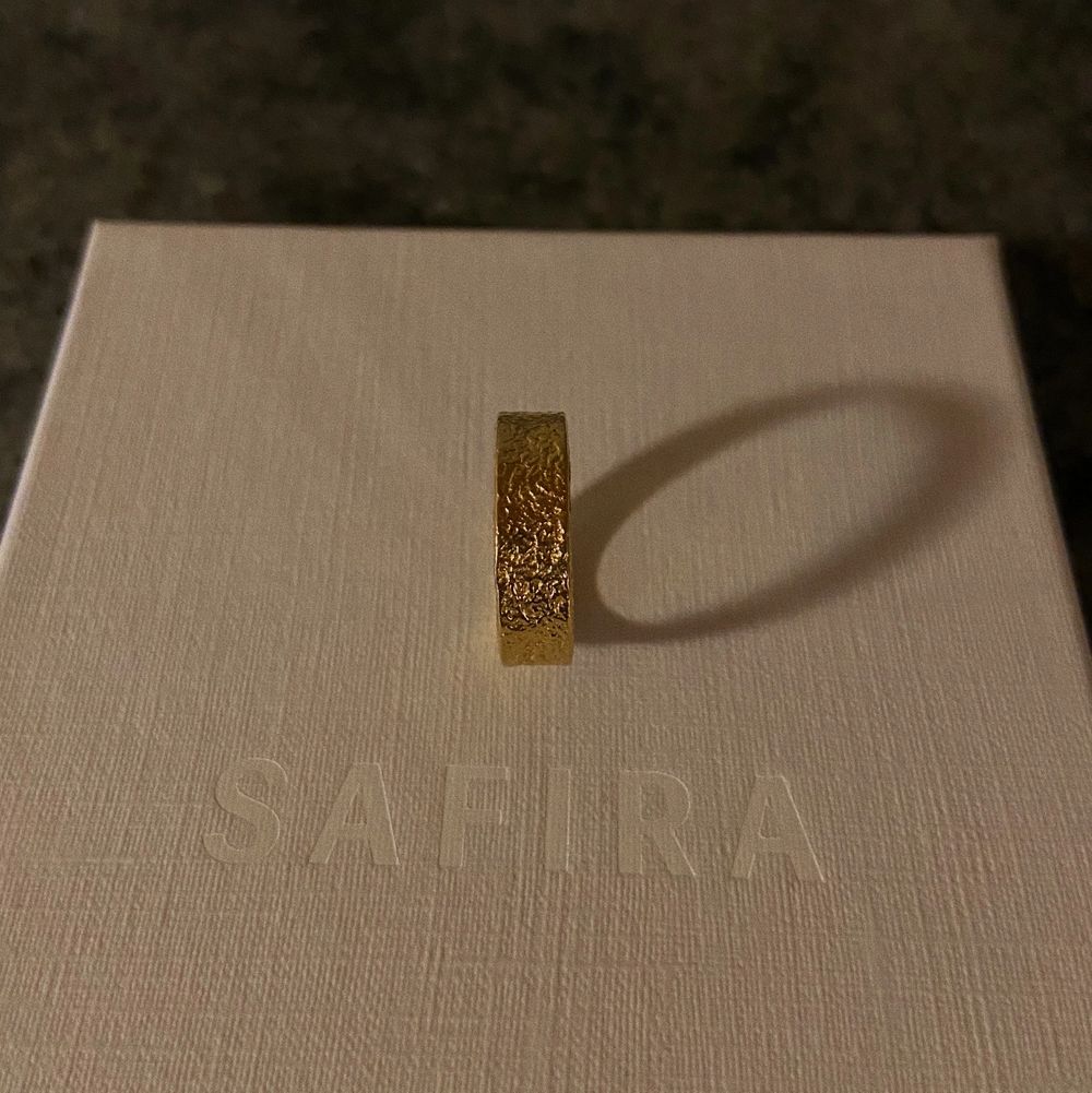 18k guldpläterad ring i äkta silver, från Safira! Ringen har en abstrakt hamrad yta med starka kontraster. Diametern på ringen är 16 mm. Helt ny, med originalbox och zip-påse. Fraktas via PostNord. (Ringen till höger på handen). Säljer denna eftersom jag har två stycken av samma ring!. Accessoarer.