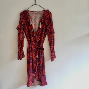 Omlottklänning strl 36/38 - Röd och blommig omlottklänning i strl 38. Jag är en 36/38 och den passar bra. Oanvänd. 