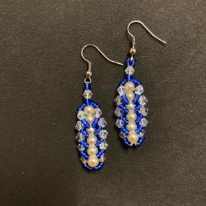 Blå och vita örhängen - Dessa örhängen har jag gjort själv.  De är gjorda av små blå glaspärlor, genomskinliga glaskristaller på kanterna och vaniljfärgade plastärlor i mitten.  Örhänget är av metal.   Själva hänget är ca 4 cm lång.   Har aldrig använt