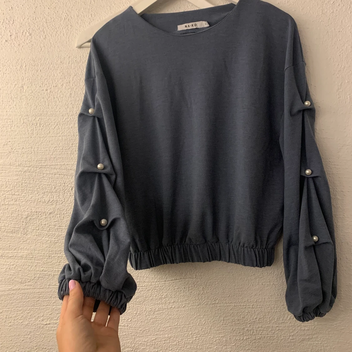 Blå tröja med pärlor på ärmarna. 