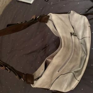 Grå Eternelväska med bruna läderdetaljer - Ganska stor grå läderväska med bruna läderband och detaljer. 