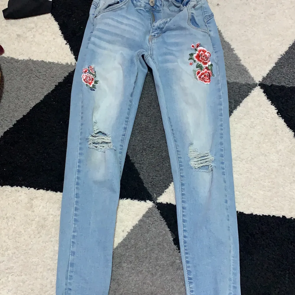 Blå jeans med hål och 2 blommor . Jeans & Byxor.