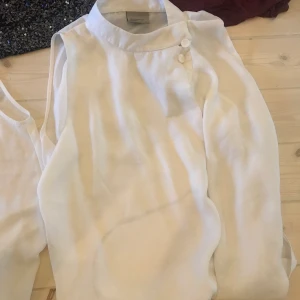 Vitt linne med krage - Vitt linne, längre modell, knappar vid halsen, omlott, knappt använt, fint skick. OBS! Strecket på linnet är inte smuts utan skugga från en sladd. 