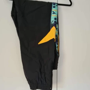 Diadora prasselbyxor - Nyproducerade prasselbyxor som använts 1-2 ggr. Bra modell med tajt ressår i midjan vilket ger den perfekta passformen runt rumpan, midjan och låren! Säljer den tillhörande jackan i en separat annons. Samfraktar gärna!