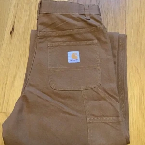 Vida byxor från carhartt - Vida byxor från carhartt med snygga detaljer på sidorna som är helt oanvända men lappen är borta, är i färg ”carhartt brown 210, storlek 16(år) men passar bra på mig som är 36/38 och 170 cm. 
