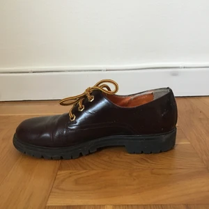 Bourgognefärgade lågskor m. gula skosnören - Retroinspirerade grova lågskor. Använda och i bra skick. Jag tycker så mycket om dem men använder för sällan för att ha kvar så jag hoppas de kan göra någon annan glad. Det står ingen storlek i men jag brukar ha 38 och de passar mig. Köpta i en vintagebutik på Östermalm. Frakten ingår inte i priset.