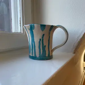En handgjord kopp i keramik med en vit underton och ljusblåa detaljer. 