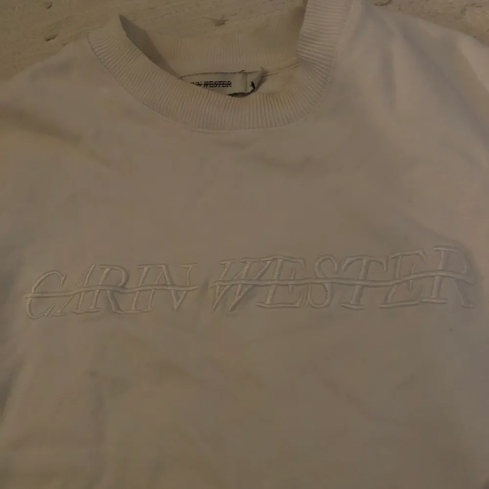Detta är en vit sweatshirt med en vit sydd text på bröstet. Tröjan är från märket Carin Wester . Tröjor & Koftor.