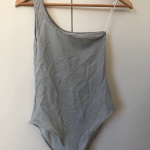 Glittrig body - Glittrig one-shoulder body från h&m. Aldrig använd så perfekt skick! Knappar i underdelen, 66kr för spårbar frakt!