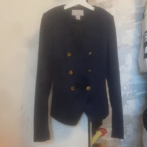 Mjuk mörkblå Kavaj HM Strl 34 - Mjuk mörkblå kavaj storlek 34. Den är otroligt stretchig men väldigt smal i axlarna! Aldrig använd så den är som ny. Insydda tjocka axelvaddar på insidan av tyget. Snygga guldiga knappar som detalj. 