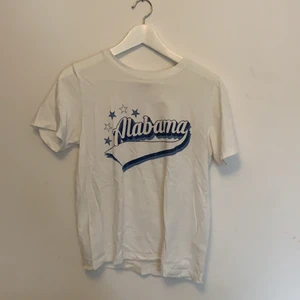 Vit t-shirt med blått tryck, storlek S - Vit t-shirt med blått tryck där det står Alabama, storlek S från ginatricot. Pris: 30kr inklusive frakt