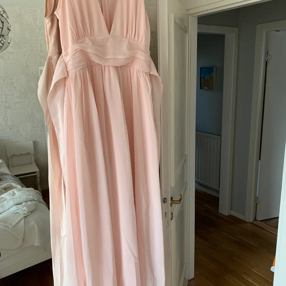 En ljusrosa balklänning från Nelly som är v-ringad, möjlighet att göra en rosett i ryggen samt en underklänning i klänningen som gör att den inte blir genomskinlig!. Klänningar.
