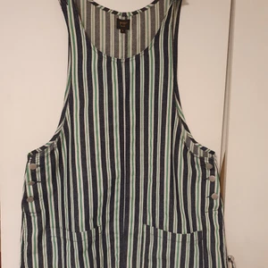 Hängselklänning I denim - En söt klänning från Pop London i ett tunnare denimtyg. Den har knappar i sidorna och på armarna samt två fickor framtill. Den är använd men i mycket gott skick. Det står storlek 4. Jag är en small-medium och på mej är den rymlig så passar nog M-L bra med.