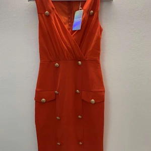 Röd klänning från Hollies - Hej! Säljer en röd figursydd klänning med guld knappar som detaljer. Aldrig använd, prislappen är kvar. Storlek S men skulle nog passa Xs också. Nypris 1200:- 