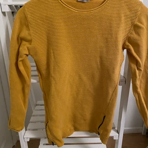 Stickad tröja - En senapsgul, stickad tröja från Kappahl. Storlek 146/152. Det finns dragkedjor längst sidorna och blir en fin detalj .