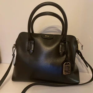 Ralph lauren väska - En fin svart läderväska från Ralph lauren. Den har två topphandtag och en lång avtagbar axelrem. En liten innerficka med dragkedja och väskan stängs med dragkedja i toppen. Nypris ca 2300kr. Väldigt fint skick!