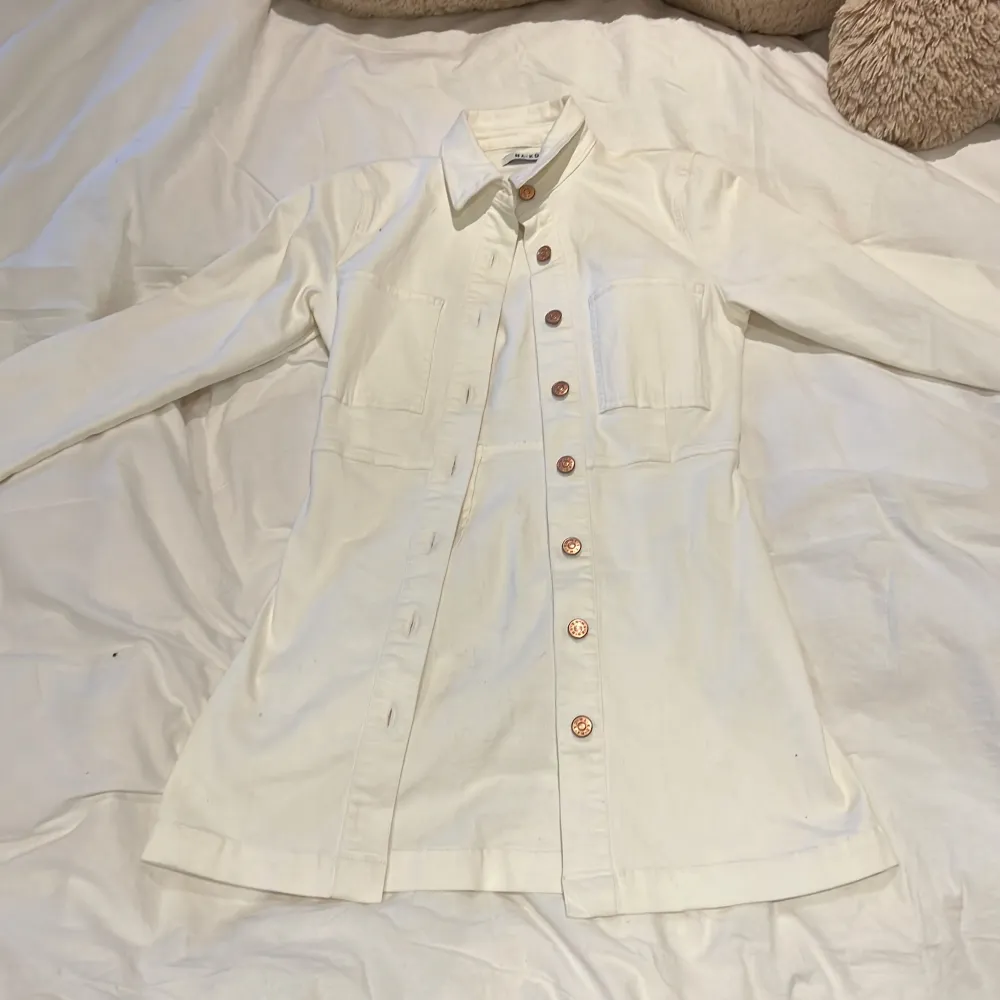 Vit lång jeansjacka/jeansklänning (kan användas till båda). Aldrig använd, köpt på NA-KD. Ord pris 499 och är helt i nyskick.😊🤍💐 på mig som är 1,63 går den ner till mitten mellan knäna och där benet börjar.🌸. Mekot.