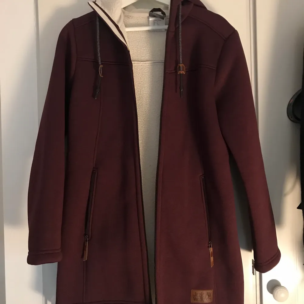 Purple long jacket from Jack Wolfskin in perfect condition, barely worn. Beautiful purple color and white warm interior lining. Great for colder weather. Brand tag on the front under the pocket and a paw tag on the sleeve. Retails for over 1000 SEK.. Jackor.