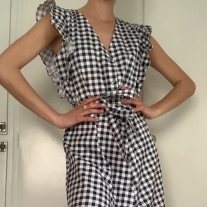 Lång rutig klänning från NA-KD - En lång supersöt rutig klänning med små volanger i ärmarna. Strl 34 men skulle absolut passa 36 med. Jag är 170cm för referens och den går ner ca 1,5 dm under knäna. Knappar hela vägen ner och ett snöre i midjan för att få extra fin passform. Använd endast en gång. Perfekt till sommaren! FRAKT tillkommer från 66kr. 