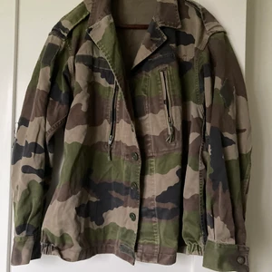 Militärjacka i grön kamouflage  - En militärjacka i grön kamouflage med amerikanska flaggan på ryggen. Storleken passar allt från S-L (i storlek S är den lite oversize och i L lite mer tight). 