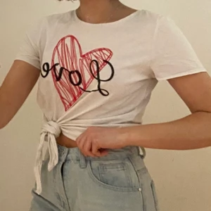 T-shirt ”Love” vit knut  - Vit T-shirt med knytdetalj fram. Stort tryck där det står ”Love” och ett rött hjärta. Haft i några år men är i bra skick och köpt i England. Det går att variera typen av knut om man vill. 100% bomull. Skönt material. Säljer pga att den inte används. Kan mötas i Umeå eller skicka om köpare står för frakt. Spårbar: 66kr, icke-spårbar: 30kr