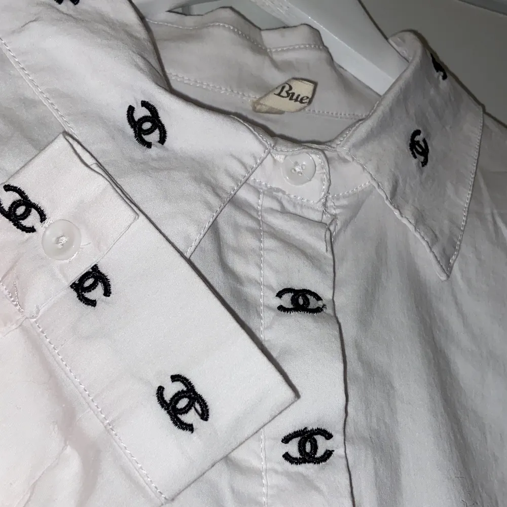 En vit skjorta med chanel mönster på sig. Den har en mindre fläck på sig på baksidan. Är i desperat behov av att bli struken. 264 = 4 ciggpaket + frakt = 323 kr. Skjortor.