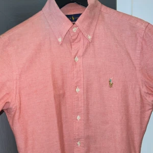 Ralph Lauren Skjorta - En extremt vacker skjorta i rosa polo skjorta som passar perfekt till stockolm stil som idag är inne otroligt vacker använt den 2 gånger i  somras och säljs på grund av att dne är för liten. Köpt för 1100kr för 2 år sedan kan vara villig att gå ner i pris