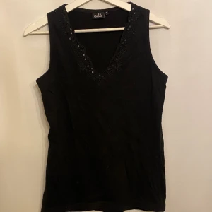 Topp med glitter - Svart topp med glitter i halsringningen. Märke: Isolde. Storlek: S 