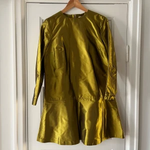 Grön klänning - En elegant grönguldig klänning med långärmad design. Klänningen har en enkel och stilren form med en lätt glansig yta. Den har en rund halsringning och en dragkedja på baksidan. Liten kjol. Väldigt kort. Köptes på vestiaire