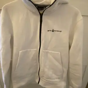 Säljer en vit zip hoodie i fint skick.  Färg: vit Märke: Sail Racing. Köparen står för frakten 