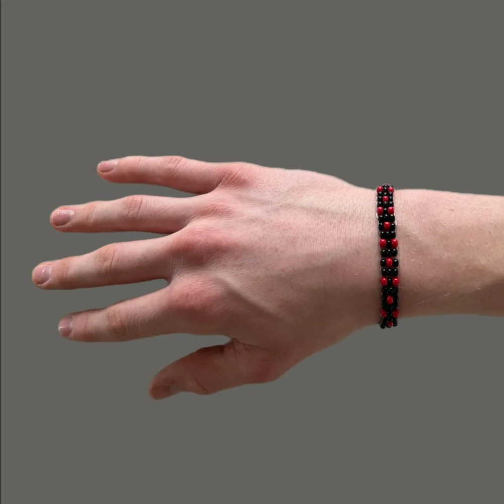 Hephaestus II Red är ett snyggt armband uppbyggt av röda och svarta rocaillespärlor. Armbandet har en omkrets på cirka 18 cm men är töjbart.. Accessoarer.