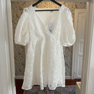 Vit klänning/ studentklänning med blommigt mönster  - Klänningen är i nyskick och har endast provats ett fåtal gånger. Säljer pågrund av att jag har hittat en annan klänning till studenten. Köpt för 999kr. 